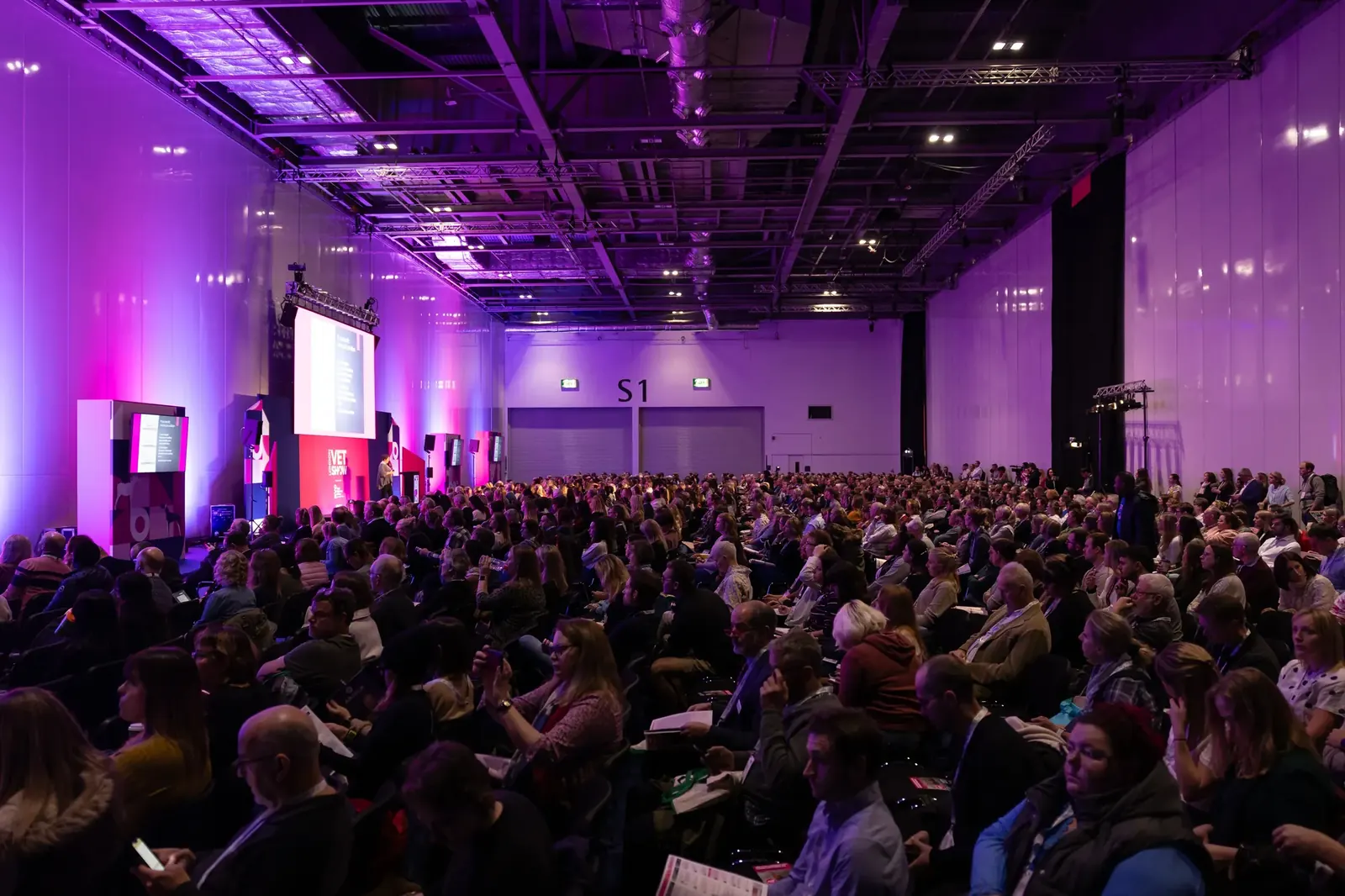 Sala de convención llena de asistentes con escenario y pantalla al fondo