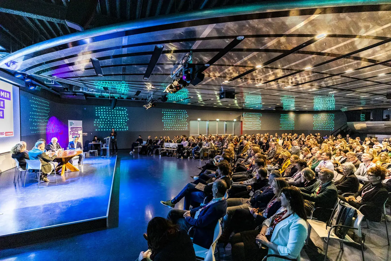 Convención de empresa con ponentes en el escenario y cientos de asistentes en la sala