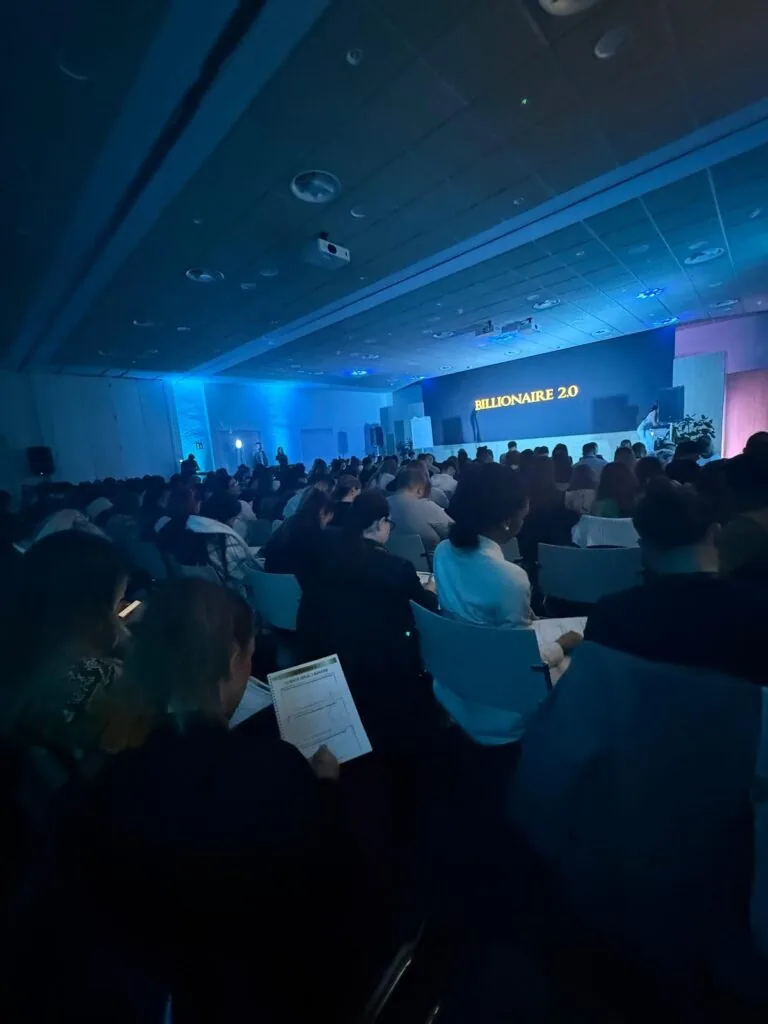 Público de Billionaire 2.0 tomando notas ante el escenario iluminado