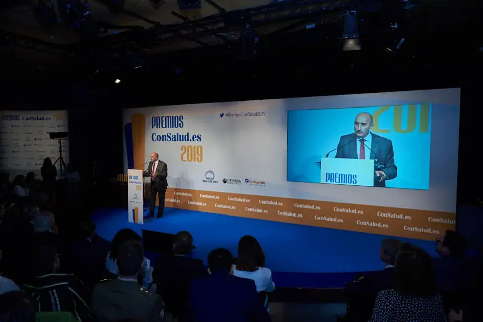 Escenario de los Premios ConSalud.es 2019 con el ponente en el atril y las pantallas