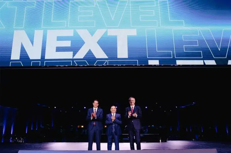 Tres directivos en el escenario bajo la pantalla LED con el lema Next Level