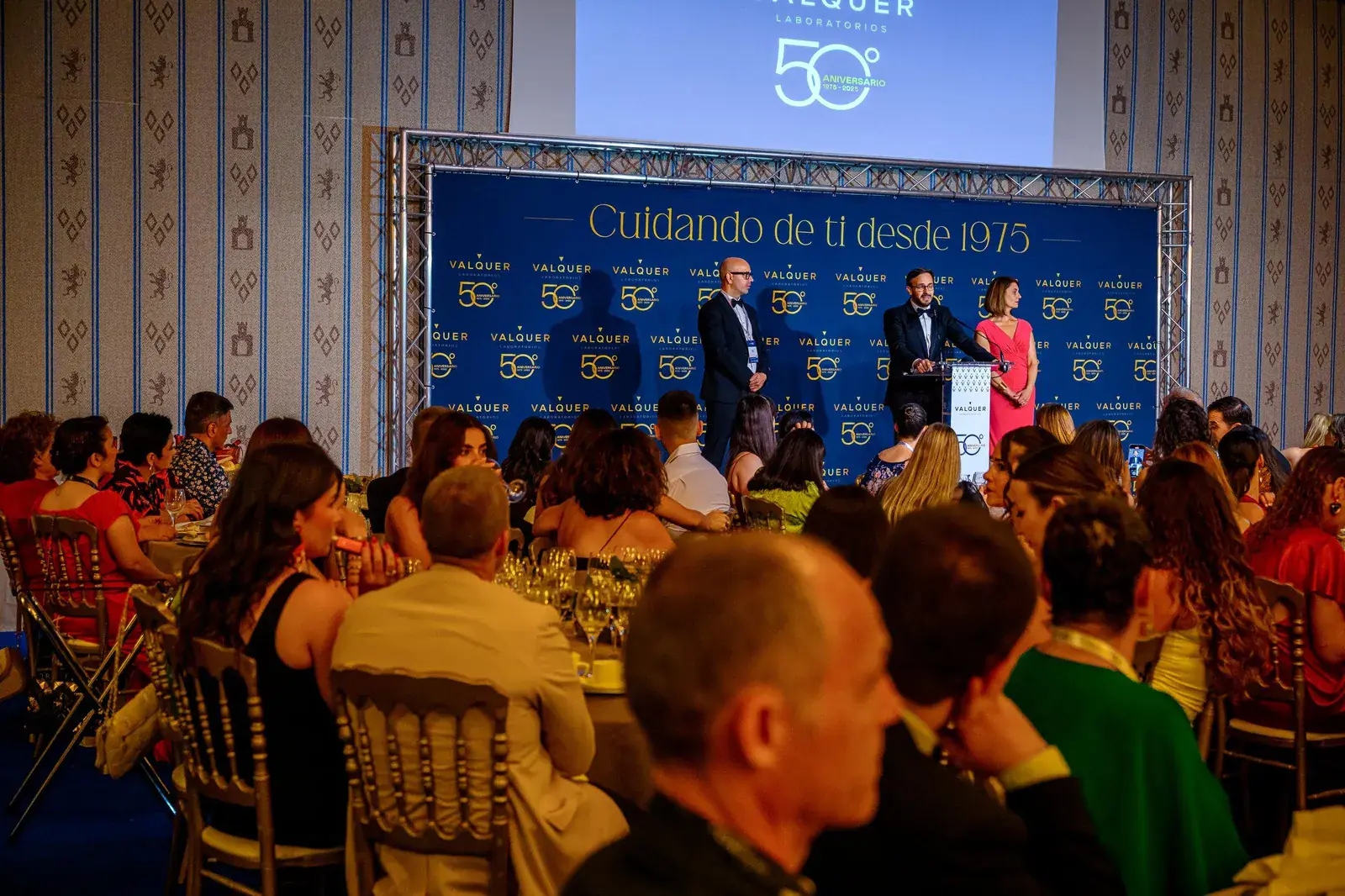 Invitados a una cena de aniversario de empresa frente al escenario con pantalla